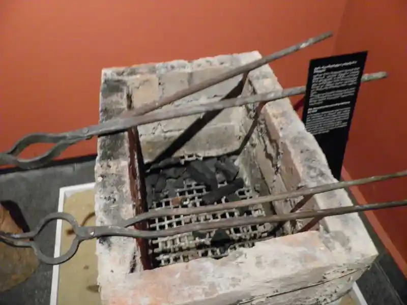 Rectangular grill made from clay bricks with metal tongs, and coals.